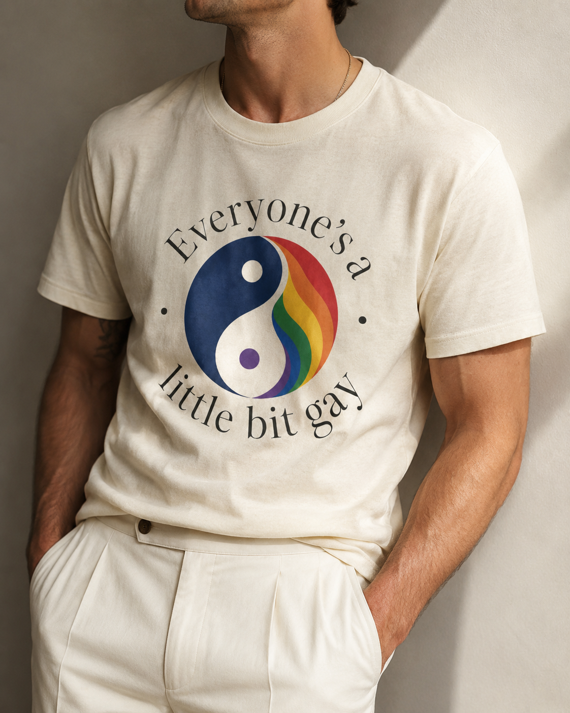 A man wearing a cream-colored t-shirt with a graphic of a yin-yang symbol split into blue and rainbow colors, with the text 'Everyone's a little bit gay' printed around it.